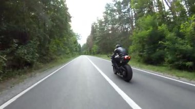 Orman yolundaki motosikletli motorcuları takip edin. Kasklı adam ormanın yakınındaki kırsal yolda modern spor motosiklet yarışı yapıyor. Yolculuk sırasında ya da yolculukta bisiklet süren adam. Özgürlük kavramı.