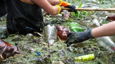Koruyucu eldivenli kadın çevrecilerin elleri enkaz nehirlerini temizliyor. Kirli gölde plastik şişe toplayan kauçuk elbiseli tanınmayan gönüllüler. Çevre kirliliği koruması.