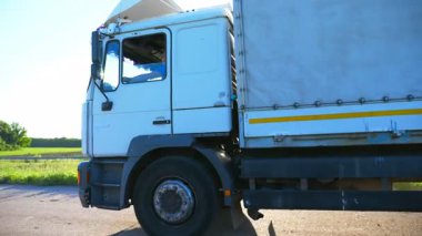 Karayolu üzerinde sürüş ve mal taşıma kargo römork ile Kamyon. Beyaz kamyon güneşli bir günde kırsal yol üzerinden hedefe sürme. Arka planda parlayan parlak güneş. Yan görünüm Yavaş hareket.