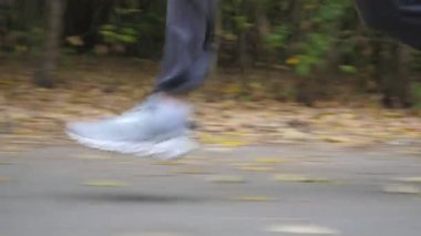 Sonbaharın başlarında ormanın yakınında yol boyunca koşan sportif bir adamın erkek ayakları. Genç atletin bacakları doğada patikaboyunca hızlı koşuyor. Dışarıda koşan güçlü bir adam. Sağlıklı aktif yaşam tarzı. Düşük görünüm.