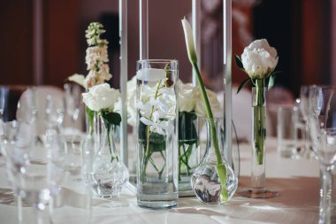 Beyaz güller, ranunculus, İran düğün çiçekleri, beyaz orkideler ve mumlar içeren geniş çiçek buketleri içeren romantik düğün masası süslemesi.