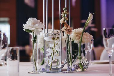 Beyaz güller, ranunculus, İran düğün çiçekleri, beyaz orkideler ve mumlar içeren geniş çiçek buketleri içeren romantik düğün masası süslemesi.