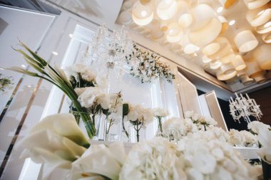 Beyaz güller, ranunculus, İran düğün çiçekleri, beyaz orkideler ve mumlar içeren geniş çiçek buketleri içeren romantik düğün masası süslemesi.