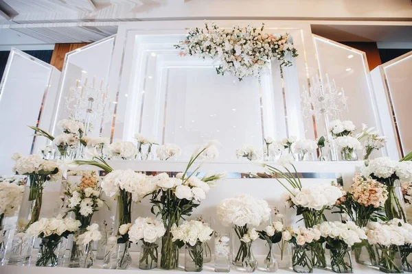 Beyaz güller, ranunculus, İran düğün çiçekleri, beyaz orkideler ve mumlar içeren geniş çiçek buketleri içeren romantik düğün masası süslemesi.