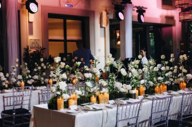 Beyaz güller, ranunculus, İran düğün çiçekleri, beyaz orkideler ve mumlar içeren geniş çiçek buketleri içeren romantik düğün masası süslemesi.