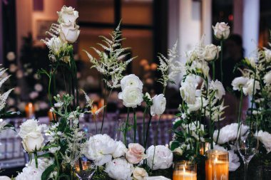 Beyaz güller, ranunculus, İran düğün çiçekleri, beyaz orkideler ve mumlar içeren geniş çiçek buketleri içeren romantik düğün masası süslemesi.