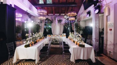 Beyaz güller, ranunculus, İran düğün çiçekleri, beyaz orkideler ve mumlar içeren geniş çiçek buketleri içeren romantik düğün masası süslemesi.