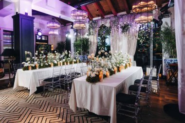 Beyaz güller, ranunculus, İran düğün çiçekleri, beyaz orkideler ve mumlar içeren geniş çiçek buketleri içeren romantik düğün masası süslemesi.