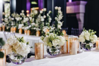 Beyaz güller, ranunculus, İran düğün çiçekleri, beyaz orkideler ve mumlar içeren geniş çiçek buketleri içeren romantik düğün masası süslemesi.