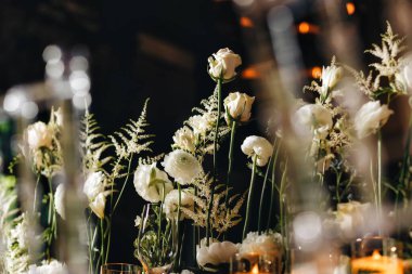 Beyaz güller, ranunculus, İran düğün çiçekleri, beyaz orkideler ve mumlar içeren geniş çiçek buketleri içeren romantik düğün masası süslemesi.