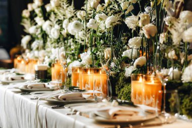 Beyaz güller, ranunculus, İran düğün çiçekleri, beyaz orkideler ve mumlar içeren geniş çiçek buketleri içeren romantik düğün masası süslemesi.