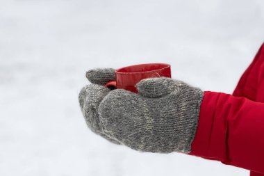 Sıcak örgü eldivenli bir adam elinde bir fincan sıcak çay tutar. Kış mevsimi kavramı, temiz havada yürür..