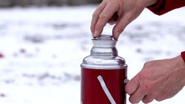 Bir adam kış ormanında termosla sıcak çay açar. Kış mevsimi konsepti..