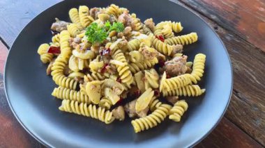 Acı biber, sarımsak, zeytinyağı ve İtalyan sosisi ile karıştırılmış ve ahşap bir masada hafif baharatlı sunulan fusili makarna yan görüntüsü. Klasik İtalyan mutfağı.