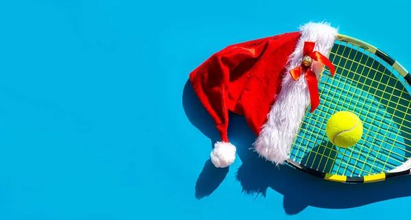 Noel Baba şapkası tenis raketinde, top mavi arka planda..