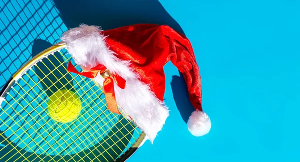 Noel Baba şapkası tenis raketinde, top mavi arka planda..