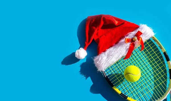 Santa Claus hat on tennis racket with ball on blue background. Stock Photo