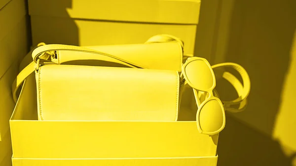 Bright illuminating yellow handbag and glasses on gray color background.