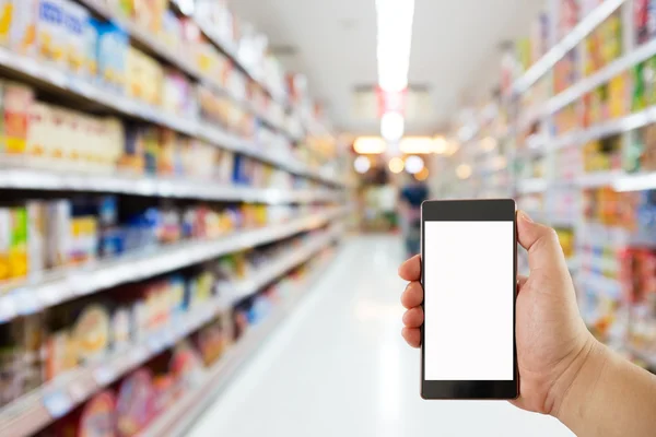 Рука тримає мобільний телефон на фоні розмиття супермаркету, бізнес-концепція — стокове фото