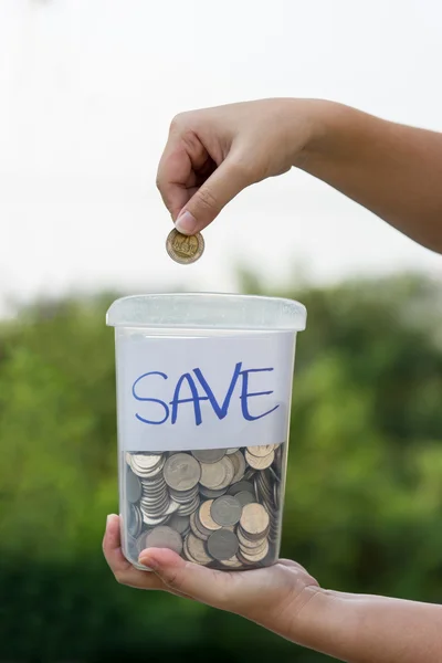 Mano femenina poniendo moneda en frasco Imágenes de stock libres de derechos