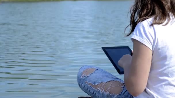 Girl uses digital tablet near the river — Stock Video