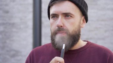 Genç adam elektronik sigara içiyor ve dumanı üflüyor.