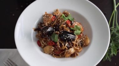 Kamera, güzel dekore edilmiş deniz ürünleri makarnasını beyaz tabakta döndürür.