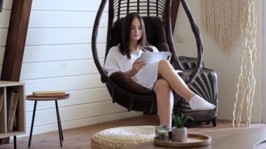 Elinde tabletle sallanan sandalyede oturan güzel bir kız.