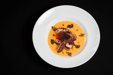 Ahtapotlu balkabağı kremalı çorba ve beyaz kasede kızarmış ekmek.