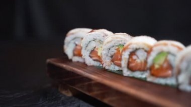 Tahta bir tahtanın üzerinde servis edilen bir dizi Japon somon suşi rulosu.