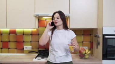 Genç ve güzel bir kız portakal suyu içiyor ve telefonda konuşuyor.