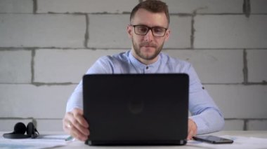 Ofiste iş istatistikleriyle çalışan gözlüklü serbest çalışan meşgul bir işçi. Mavi gömlekli adam işe koyuluyor.