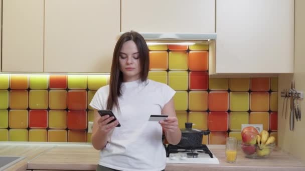 Egy Gyönyörű Lány Mobiltelefonnal Hitelkártyával Kezében Online Rendelést Tesz Konyhájában — Stock videók