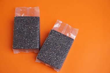 Siyah pirinç süpürgesi parlak turuncu arka planda, şeffaf plastik poşetlerde paketlenmiş. Sağlıklı organik gıda kavramı, kaliteli Tayland pirinç ambalajı ve reklam ve pazarlama kullanımı için temiz ürün sunumu.                               