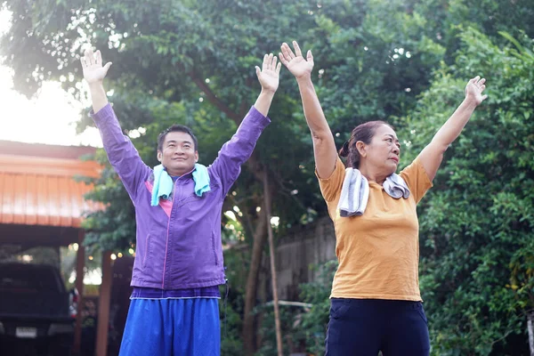 Yaşlı Asyalı kadın ve orta yaşlı adam kollarını kaldırarak dışarıda egzersiz yapıyor, sabah esneme hareketlerinin keyfini çıkarıyorlar. Kavram, aktif yaşlanma, kıdemli fitness, sağlıklı bakım ve sağlıklı yaşam tarzı aktivitesi.                               