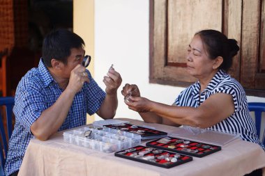   Asyalı son sınıf öğrencisi bir kadın ve orta yaşlı bir Asyalı adam Budist tılsımını dikkatle inceliyor, büyüteç kullanıyorlar. Masa tılsım koleksiyonlarıyla dolu, odak ve ortak ilgi alanları gösteriyor. Hobi.                             