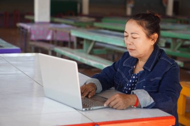 Masada dizüstü bilgisayar kullanan kıdemli Asyalı kadın. Çevrimiçi çalışan yaşlı kadın, öğrenme teknolojisi, uzaktan çalışma yaşam tarzı, dijital iletişim, aktif yaşlanma ve modern son sınıf konsepti.