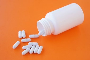 Beyaz kapsül hapları parlak turuncu arka planda plastik bir ilaç şişesinden dökülüyor. Eczacılık ilaçları, vitaminler, takviyeler, tıbbi tedavi, dozajı gösteren minimum sağlık konsepti.