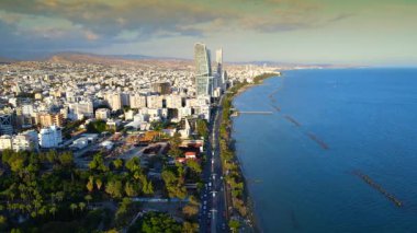 Kıbrıs Rum Kesimi 'nin Limasol kentinin hava panoramik manzarası, modern ufuk çizgisi, yerleşim alanları ve yeşil alanları vurguluyor. Görüntü canlı şehir yaşamını, kentsel gelişimi ve Akdeniz kıyı atmosferini yansıtıyor..