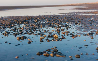 Kum dalgaları, kumsal taşları ve gökyüzünün su havuzuna yansıdığı güzel, güneşli bir İngiliz kumsalında kış günü..