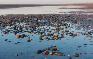 Kum dalgaları, kumsal taşları ve gökyüzünün su havuzuna yansıdığı güzel, güneşli bir İngiliz kumsalında kış günü..