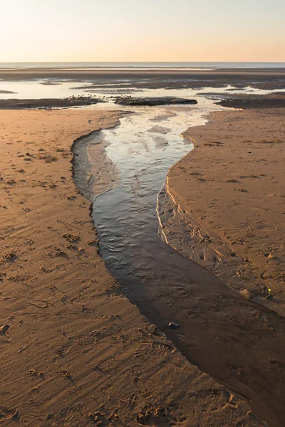 Vackra soliga vinterdag på en brittisk strand, med en ström som leder ut till havet. — Stockfoto