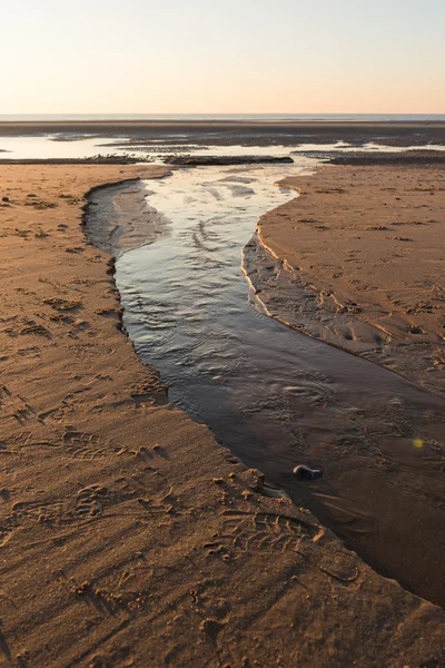 Vackra soliga vinterdag på en brittisk strand, med en ström som leder ut till havet. — Stockfoto