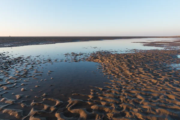 Vackra soliga vintrar dag på en brittisk strand, med sand ringar, strandstenar och himlen reflekteras i en vattenpool. — Stockfoto