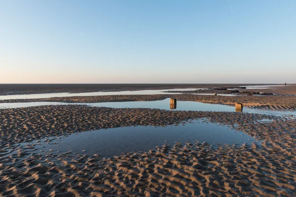 Vackra soliga vintrar dag på en brittisk strand, med sand ringar, strandstenar och himlen reflekteras i en vattenpool. — Stockfoto