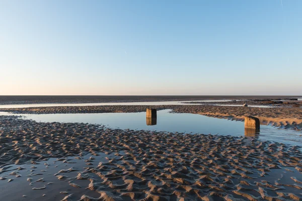 Vackra soliga vintrar dag på en brittisk strand, med sand ringar, strandstenar och himlen reflekteras i en vattenpool. — Stockfoto