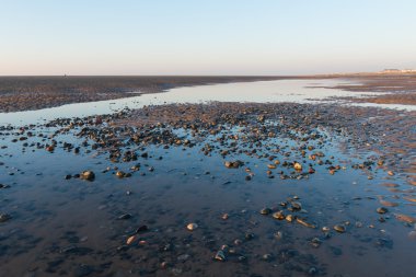 Kum dalgaları, kumsal taşları ve gökyüzünün su havuzuna yansıdığı güzel, güneşli bir İngiliz kumsalında kış günü..
