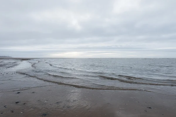 Avkopplande och mild lugnande vågor flyter in i en strand på en dyster mulen dag — Stockfoto