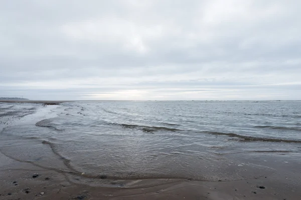 Avkopplande och mild lugnande vågor flyter in i en strand på en dyster mulen dag — Stockfoto