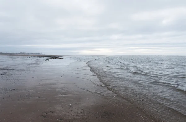 Ondas calmantes relaxantes e suaves que fluem para uma praia em um dia sombrio nublado — Fotografia de Stock